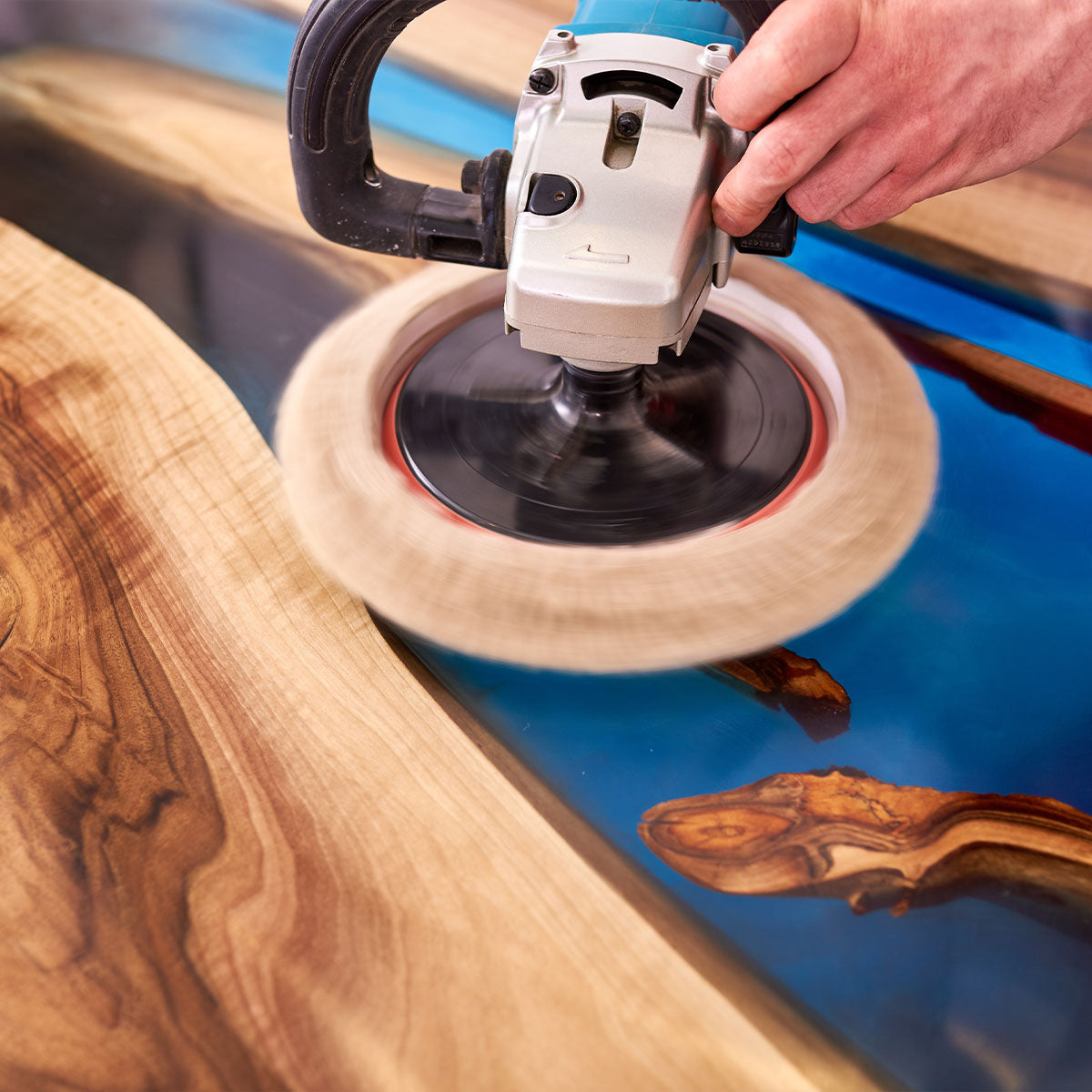 Power buffer polishing a wood and blue resin tabletop, highlighting the wood's natural grain and glossy resin surface.