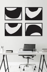 Four black and white abstract canvas prints with organic curved shapes arranged in two rows above a modern white desk and black office chair in a minimalist room.