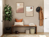 Neutral-toned entryway with two abstract framed canvases above a wooden bench holding a patterned beige pillow and stacked books beside woven baskets on the floor.