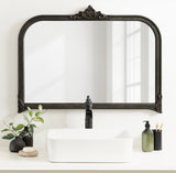 Rectangular wall mirror with curved top and ornate black frame featuring intricate floral detailing, above a white rectangular vessel sink and black faucet.