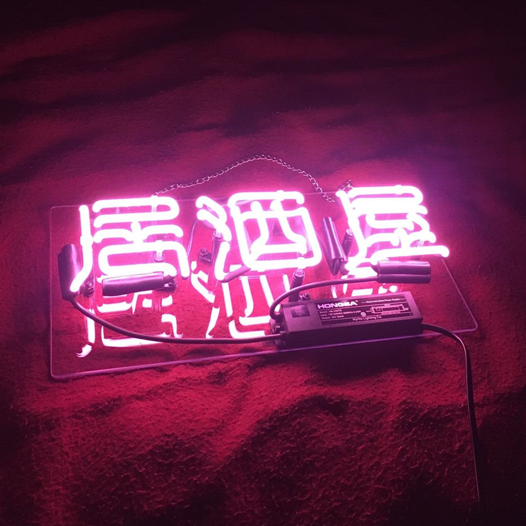 Bright pink neon sign with Chinese characters for 'Izakaya' Japanese bar on a textured dark red surface with visible wiring and power supply below the sign.