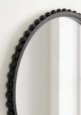 Close-up of a round wall mirror with a black frame featuring evenly spaced spherical bead accents around its edge against a white wall.