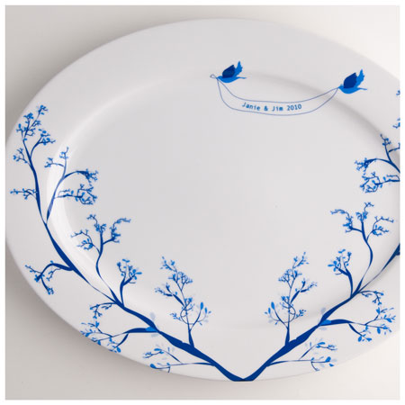 White oval ceramic platter decorated with blue branches and two blue birds holding a banner that reads 'Janie & Jim 2010' near the rim.