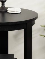 Black round wood side table with a smooth matte finish, showing three straight legs and two white circular marble coasters on top beside a black candlestick.