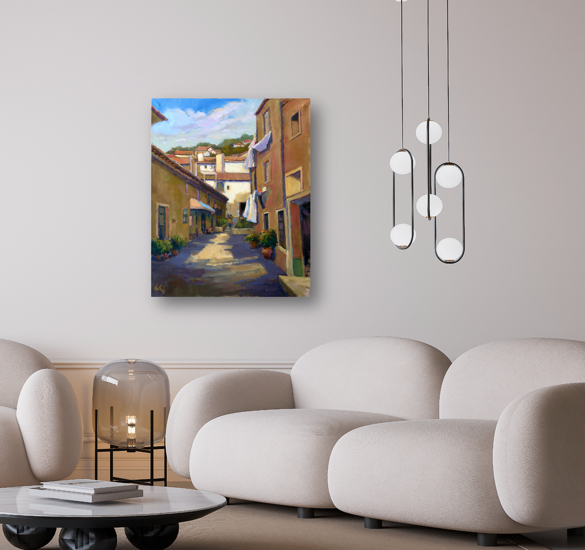 Painting of a sunlit narrow alley with warm brown buildings, green plants, and a blue sky with white clouds, displayed on a beige wall above a cream sofa.