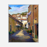 Sunlit narrow alley with terracotta and beige buildings, potted plants along the street, and white laundry hanging from windows against a blue sky.