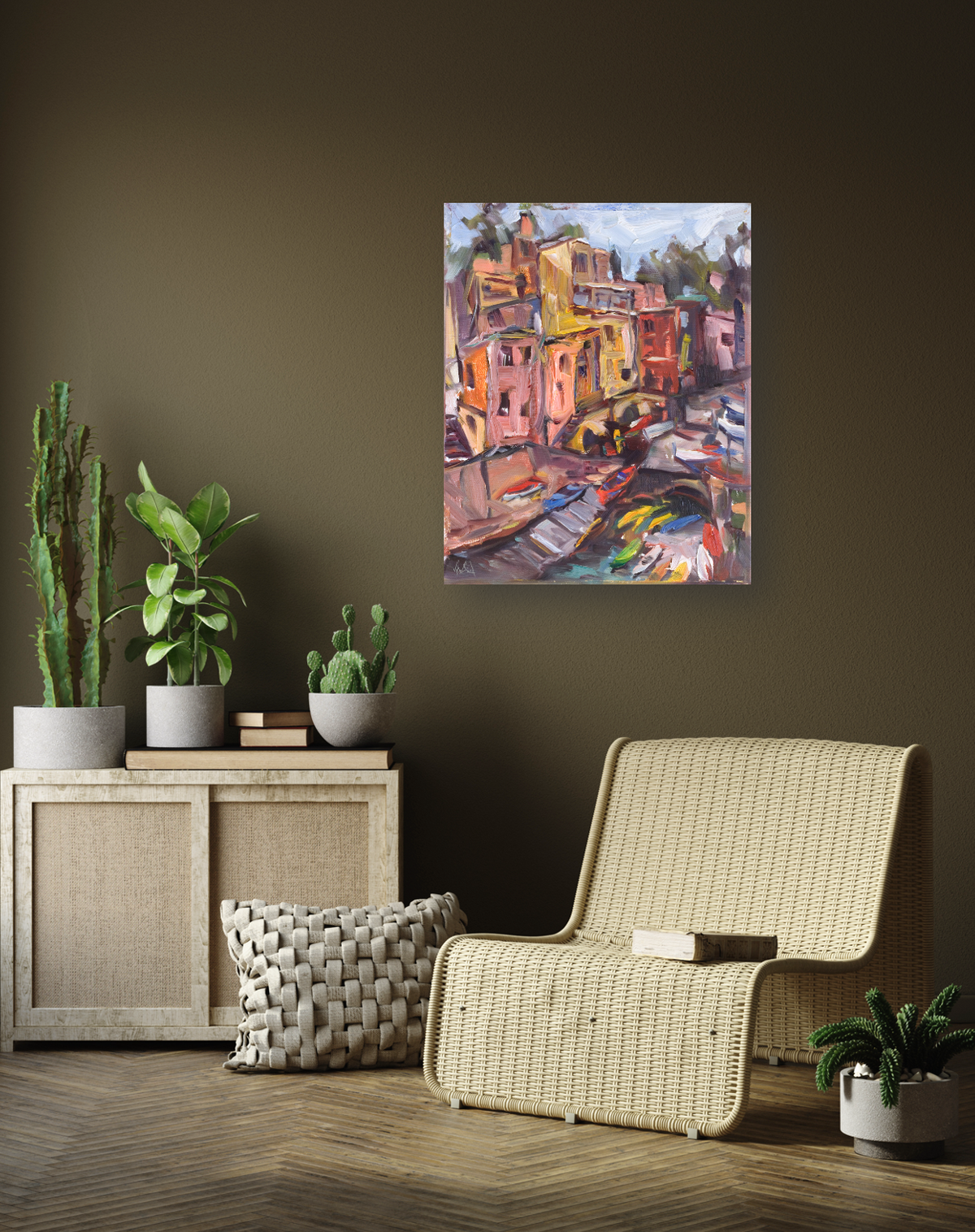 Colorful canvas print of a vibrant Italian coastal village with boats, displayed on a dark olive wall above a wicker chair and wooden cabinet with potted plants.