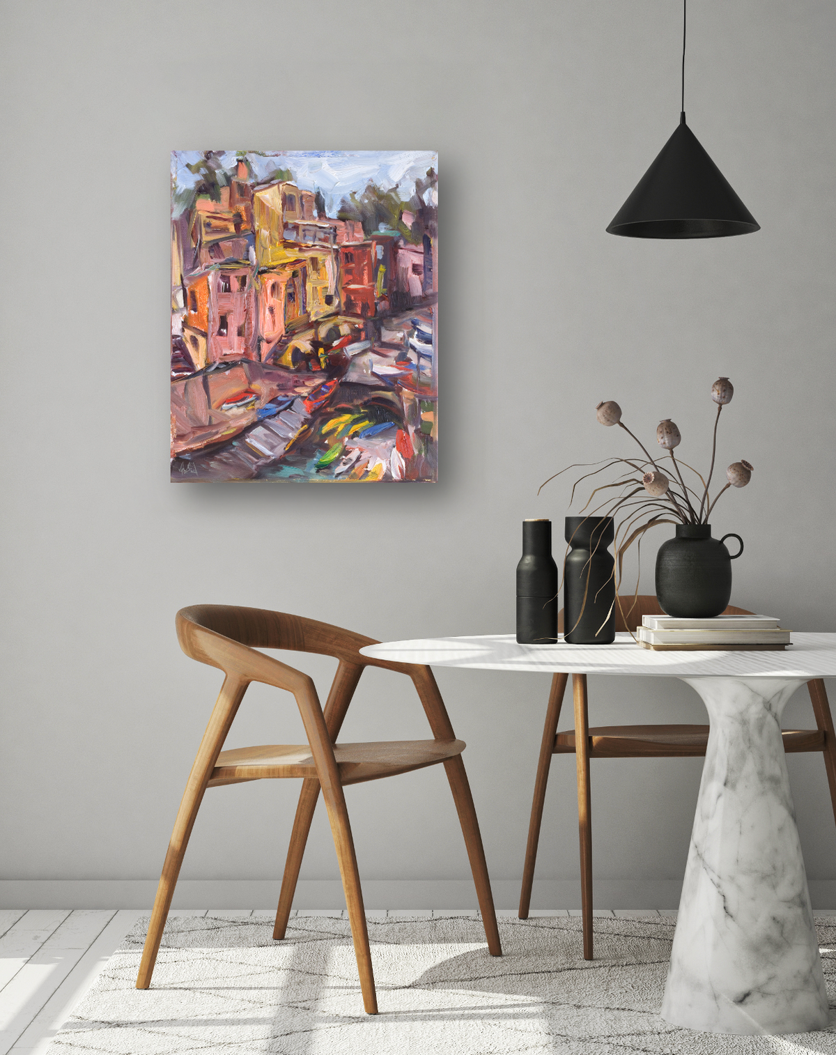 Abstract colorful painting of multi-story buildings near a canal with boats, displayed on a light gray wall above a white marble table and wooden chair.