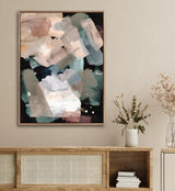 Abstract canvas with layered brushstrokes in muted beige, green, and blue tones against a black background, framed with small bead detailing, hung over a wooden cabinet.