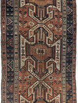 Narrow rug with three large geometric shield motifs in rust, cream, and dark blue, surrounded by multiple borders featuring small floral and diamond patterns.