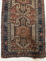 Pre-1900 Sewan Kazak rug with triple shield pattern in rust, cream, and navy blue, featuring geometric motifs and a wide border with triangular designs.