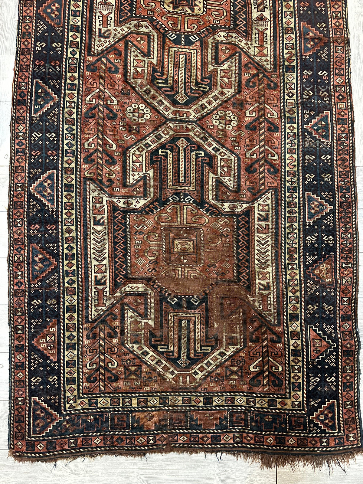 Pre-1900 Sewan Kazak rug with triple shield pattern in rust, cream, and navy blue, featuring geometric motifs and a wide border with triangular designs.