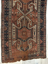 Antique Sewan Kazak rug with geometric triple shield motifs in rust, cream, and dark blue, bordered by repeating triangular patterns, showing wear at one end.