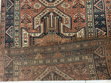 Section of a pre-1900 Sewan Kazak rug featuring a large triple shield medallion in muted reds, deep blues, and ivory with geometric motifs and floral patterns.