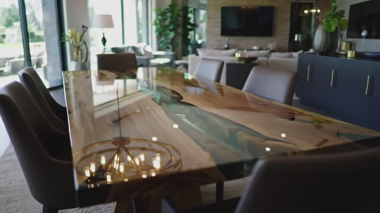 Load video: A luxury walnut wood dining table with clear epoxy river detail. The camera slowly pans across the tabletop, highlighting the smooth resin finish, natural grain patterns, and handcrafted design. Light reflections dance on the surface, showcasing the elegance and craftsmanship of the piece.