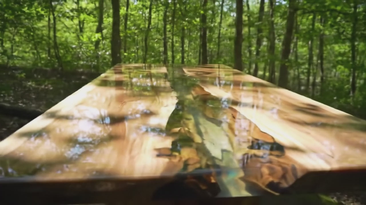 Load video: A luxury walnut wood dining table with deep epoxy resin river detail. The camera slowly pans across the tabletop, highlighting the smooth resin finish, natural grain patterns, and handcrafted design. Light reflections dance on the surface, showcasing the elegance and craftsmanship of the custom dining table