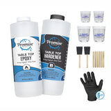 Two 32 oz bottles labeled Promise Table Top Epoxy and Hardener with mixing cups, foam brushes, wooden stir sticks, and black gloves arranged on a white background.