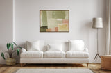 Abstract painting with blocks of green, beige, pink, and brown hues framed above a white three-seat sofa with two matching cushions, flanked by a potted plant and tall floor lamp.