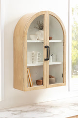 Wall-mounted wooden cabinet with an arched top, featuring two glass-paneled doors with black handles and white interior shelves holding minimalistic ceramics.