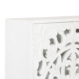 Close-up of a white wooden wall cabinet corner featuring intricate carved floral and scroll patterns with a distressed finish on the door panel.