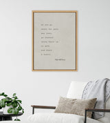 Framed Sylvie Emerson quote in simple black type on beige canvas, hanging above a white armchair with gray blanket and brown pillow, near a small green potted plant.