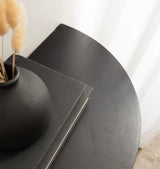 Close-up of a dark matte-finished floating wood side table with a rounded edge, featuring a textured black vase and stacked black books.