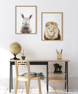 Minimalist desk with light wood chair, globe, and small plant beneath two framed animal portraits: a white rhinoceros and a lion with a full mane.