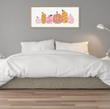 Rectangular framed canvas above bed depicting six stylized pumpkins in pink, orange, and mustard tones with leaf and vine patterns on white background, set against gray wall.
