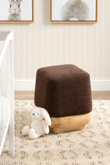 Square ottoman with a soft, dark brown fabric top and a light wood base, placed on a patterned beige rug beside a white crib and a stuffed white bunny toy.