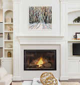 Abstract painting of a snowy forest with tall, leafless trees and colorful shadows, framed above a modern white fireplace with a burning fire.