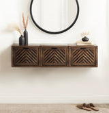 Wall-mounted dark wood floating side table with three geometric chevron-patterned doors beneath a round black-framed mirror, decorated with black vases and dried grasses.
