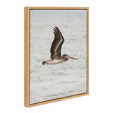 Framed canvas showing a brown pelican in mid-flight over a calm water surface with soft gray and green tones, captured from side profile.