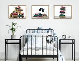 Black metal bed with white bedding and blue and gray decorative balls, flanked by black side tables holding a plant and clock, below three framed vintage vehicle pile prints