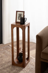 Tall, narrow rectangular wood table with rounded cutout sides, holding a framed black-and-white sketch and a black mug, beside a sofa on a textured rug.