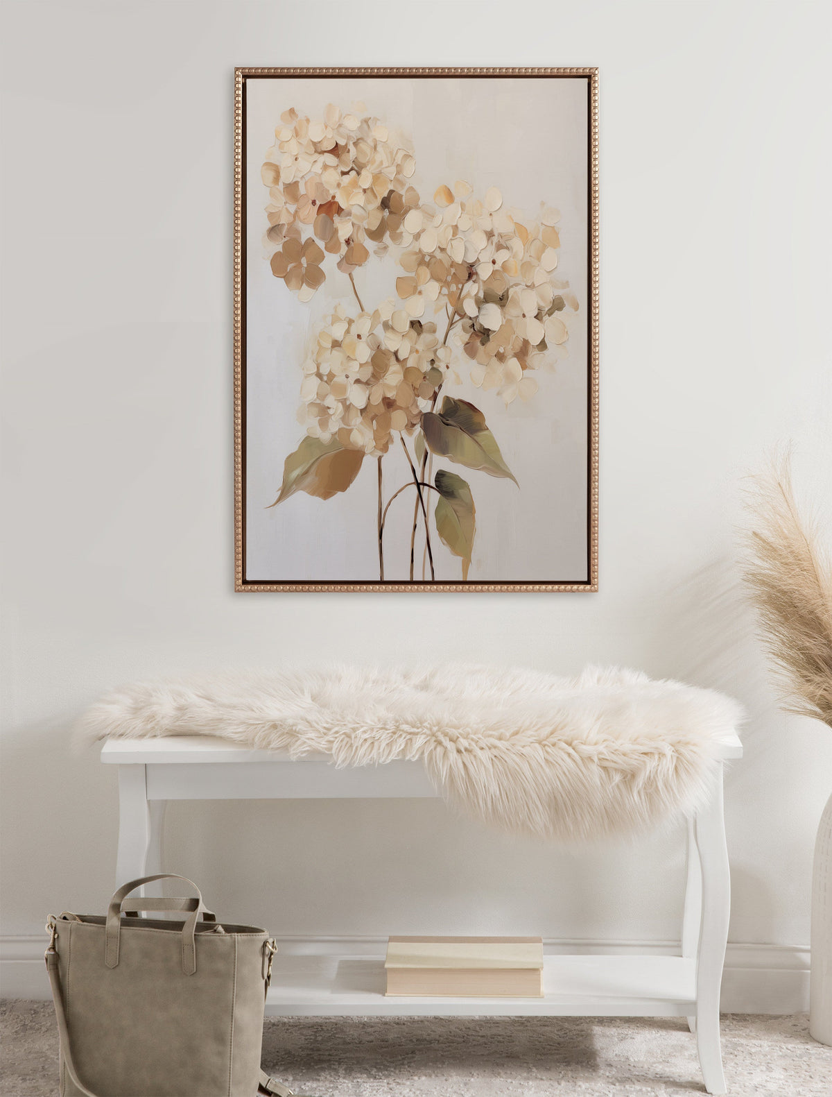Framed canvas artwork depicting soft beige hydrangea flowers with green leaves, hung above a white bench draped with a fluffy cream throw in a neutral-toned room.