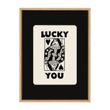 Black and white framed print featuring a stylized Queen of Spades playing card with the words 'LUCKY YOU' above and below the card on a black background.