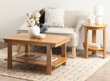 Rectangular wooden coffee table with straight legs and lower shelf, paired with a beige upholstered sofa and round wood side table with lamp and books.