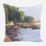 Pillow with impressionist-style landscape painting featuring a riverbank with green trees, brown earth, and soft gray-blue sky reflections in the water.