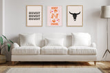 Three framed artworks above a white cushioned sofa with wooden legs: left text repeating 'Howdy', center colorful cowgirl with pink and orange hues, and right black bull skull silhouette.
