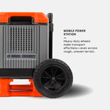 Close-up of a mobile power station's large black heavy-duty wheel and gray vented body with orange accents, highlighting its transport ease over rough terrain.
