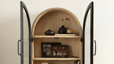 Arcott Arch Wall Cabinet with arched top and black metal frame doors, displaying black and gold vases and framed photographs on cream-colored shelves.