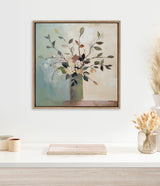 Square framed canvas of watercolor-style floral bouquet with varied leaves in muted greens, browns, and blues on blended background, hanging above minimalist white shelf.