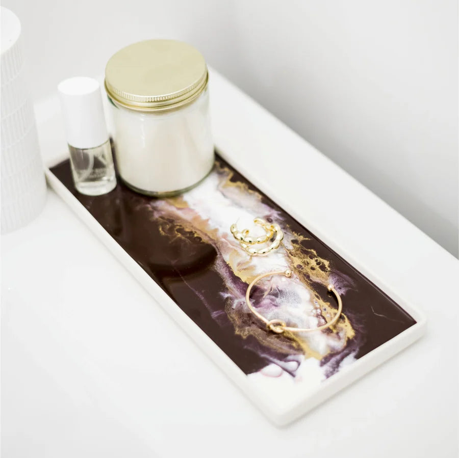 Decorative resin ceramic tray with gold jewelry, candle, and small bottle on a white surface