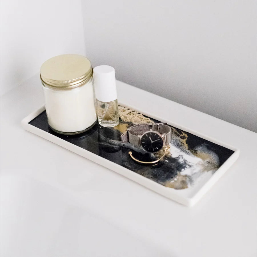 White resin ceramic tray with a candle, small bottle, and watch on a light gray surface.
