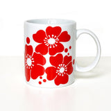 White porcelain mug decorated with large, bold red flowers with white centers and small red dots scattered between them.