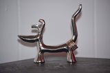Silver-finished dog-shaped ring holder with a long curved tail holding a textured ring, standing on four short legs against a plain background.