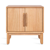 Compact square side table with two wooden doors and vertical rounded wooden handles, standing on four tapered legs in light natural wood finish.