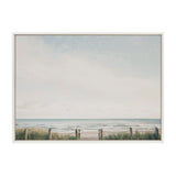 Framed canvas print showing a calm beach scene with a light blue sky, distant ocean waves, and sandy shore bordered by grassy dunes and wooden posts linked by rope.