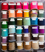 Thirty spools of colorful thread arranged in six rows, each labeled with colors like red, neon pink, olive, royal blue, purple, and creamy white in a storage container.