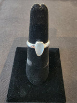 Silver ring with a polished teardrop-shaped aquamarine stone set on a black velvet ring holder against a dark fabric background.